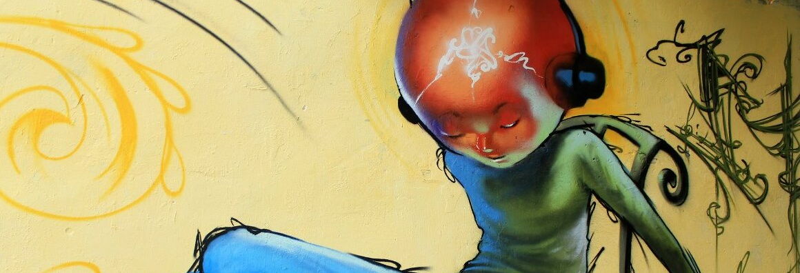 Graffiti of a character with a large orange and red head in a green long-sleeved shirt with headphones on their ears against a yellow background.