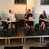 Die Sprecher*innen sitzen auf einem Podium vor Publikum in einem Innenhof. Nebiha Guiga spricht in ein Mikrofon.