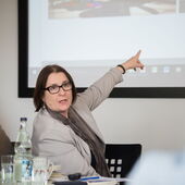 Irina Scherbakowa spricht und zeigt auf eine Leinwand im Hintergrund.