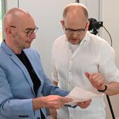 Claude Haas und Stefan Willer beugen sich über ein Blatt Papier in Haas' Händen und unterhalten sich.