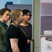 Three participants stand in front of two posters