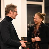 Two people are standing next to each other and are having a conversation. Both are smiling.