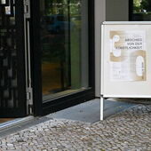Aufsteller mit dem Veranstaltungsplakat vor der geöffneten Tür zum Konferenzraum.