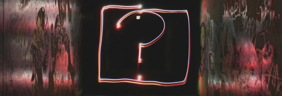Glowing question mark made of red and white light trails inside a dark, graffiti-covered tunnel.