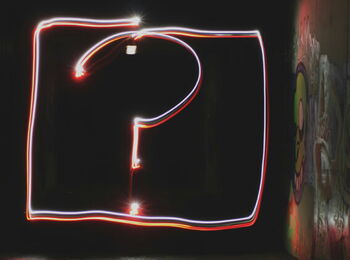 Leuchtendes Fragezeichen aus roten und weißen Lichtspuren in einem dunklen, mit Graffiti besprühten Tunnel.