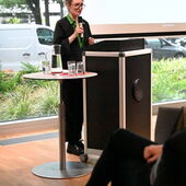 Hanna Hamel steht am Rednerpult und spricht. Hinter ihr eine Präsentation mit einem Zitat von Max Bense.