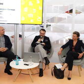Zaal Andronikashvili moderiert ein Gespräch mit Giga Zedania und Eva Geulen. Alle drei sind in der Frontansicht zu sehen und sitzen auf einem Podium vor einem Bildschirm.