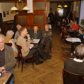 Halina Hackert reads aloud while the audience sits at various small tables with cups and plates and listens