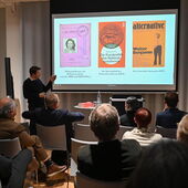 Moritz Neuffer steht vor einer Leinwand, auf der der Pass von Hildegard Brenner, eines ihrer Buchcover und ein Coverblatt der Zeitschrift »alternative« zu sehen sind.