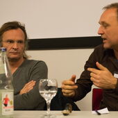 Torsten Michaelsen and Philip Scheffner are sitting at a conference table. Philip Scheffner speaks and gestures.
