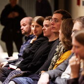 Eine Reihe mit sieben Personen, die der Podiumsdiskussion lauschen und nach vorne schauen.
