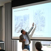Andreas Ludwig stands in front of the screen and points with his arm to his presentation, which shows a street view and a development plan for a section of West Berlin’s north-south axis from the 1960s.