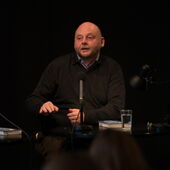 Thomas Hettche sits in front of a black background at a microphone and speaks