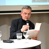 Christoph Hesse liest aus einem Buch vor und spricht dabei ins Mikrofon.