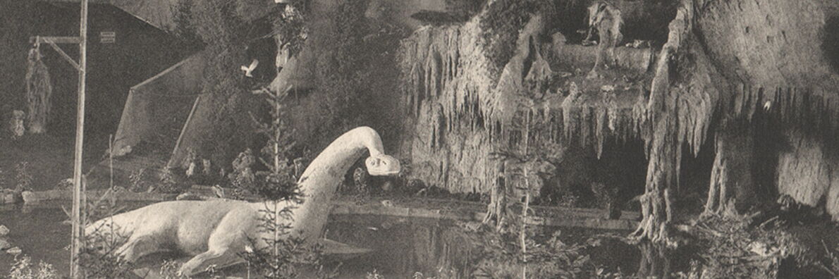 Historische Schwarzweiß-Inszenierung einer urzeitlichen Landschaft mit Dinosauriermodell zwischen künstlichen Felsen, Tannen und kleinem Teich in einem Innenraum.