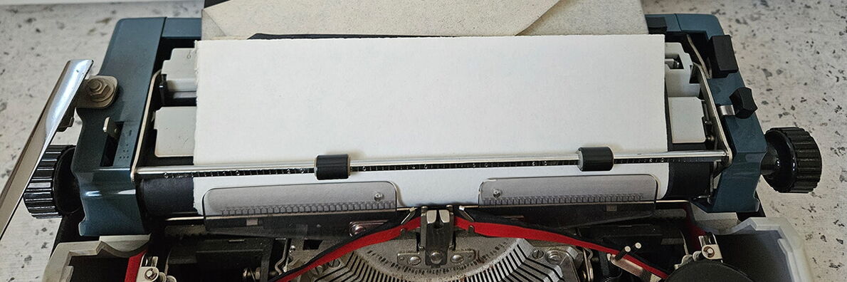Close-up of a typewriter with a blank sheet of paper inserted and the ink ribbon visible.