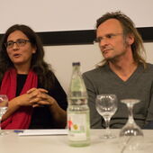 Philip Scheffner und Merle Kröger sitzen an einem Konferenztisch vor einer Leinwand.