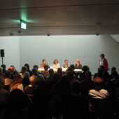 In the foreground is a crowd of people, in the background the four authors and another woman can be seen.