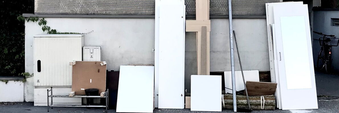 Various pieces of furniture are leaning against a wall on a sidewalk on a street with a gully.