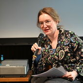 Hanna Hamel speaks into a microphone, she holds two pieces of paper in her hand.