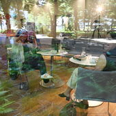 Durch ein Fenster, in dem sich Pflanzen und die Straße spiegeln, sind Sonja Longolius und Lin Hierse zu erkennen, die im Veranstaltungsraum sitzen.