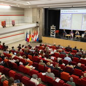 Auditorium und Podium aus der Vogelperspektive. Auf dem Podium sitzen fünf Personen.