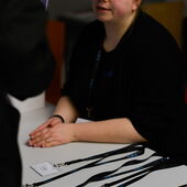 An event staff member is sitting at a table with name tags on display. She is talking to someone at the table