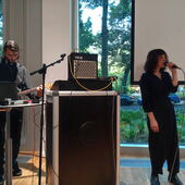 Sveta Ben und Syarhey Navitsky stehen vor der Leinwand. Er spielt Gitarre, sie singt.