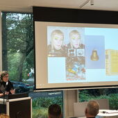 Olga Bubich steht am Rednerpult und spricht zum Publikum. Auf der Leinwand neben ihr sind mehrere Fotos und Instagram-Screenshots zu sehen.