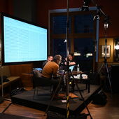 The authors Philipp Schönthaler and Hannes Bajohr and the moderator Morten Paul are sitting on a podium. Behind them is a large screen with indecipherable rows of text.