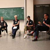 Katrin Trüstedt, Birgit M. Kaiser, Kathrin Thiele, and Daniel Loick are sitting in a semicircle in front of a green board in the lecture hall. Daniel Loick speaks into the microphone, the others look at him or at their notes.