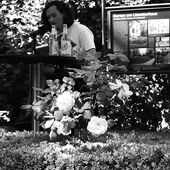 Joshua Groß sitzt an einem Tisch und liest vor. Vor ihm wächst eine Rose.