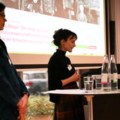 Gianna Zocco und Sandra Folie stehen am Pult. Folie spricht, Zocco schaut sie an.