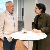 Karl Schlögel and Shira Miron are standing at a bistro table with cups on it, chatting.