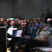 Blick von der Straße in den Veranstaltungsraum, es sind voll besetzte Publikumsreihen zu sehen.