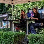 Janika Gelinek and Heike Geißler sit together on a stage. Heike Geißler reads from her book “Die Woche,” Janika Gelinek listens to her attentively.