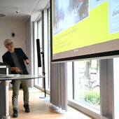 Michael Bienert stands at the lectern and turns to the presentation behind him.