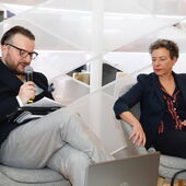 Zaal Andronikashvili spricht in ein Mikrofon, Eva Geulen hört ihm zu. Auf dem Tisch vor ihnen steht ein Laptop.