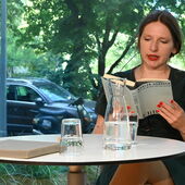 Marlen Hobrack sitzt an einem weißen Bistrotisch und liest aus ihrem Roman »Erbgut«.