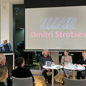 Andreas Weihe stands at the microphone and speaks, Dmitri Strotsev, Tatsiana Kupreichyk, and Nina Weller sit to his right, facing each other.