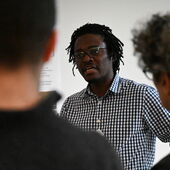 Burrhus Njanjo spricht zum Publikum, das unscharf von hinten zu sehen ist.