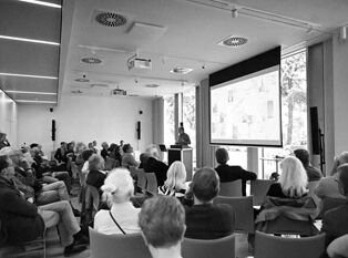 Vortragssaal mit ca. 50 Personen im Publikum, die in Richtung Leinwand und dem vortragenden Martin Germer schauen.