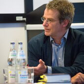 Daniel Weidner sits on a chair, he looks to the right and gestures with his left hand.