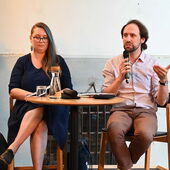 Kaja Skowrońska and Sébastien François sit on a podium, Sébastien François speaks into a microphone.