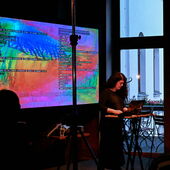 Alexandra Cárdenas steht auf einem Podium vor ihrem Laptop. Hinter ihr ist eine bunte Leinwand mit unleserlichem Text zu sehen.