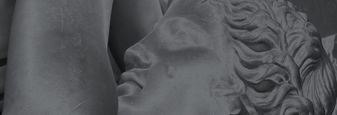 Black and white photograph of a Greek statue, detail: profile of a figure with wavy hair and left arm stretched upwards.