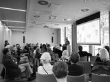 Vortragssaal mit ca. 50 Personen im Publikum, die in Richtung Leinwand und dem vortragenden Martin Germer schauen.