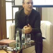 Giorgi Maisuradze sitzt auf einem Sessel vor einer Leinwand und spricht.