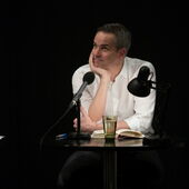 Stephan Thome sits at a microphone, props his chin in his hand and looks up