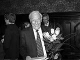 Black and white photograph of Eberhard Lämmert on his birthday. He holds flowers in his hand and smiles.